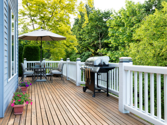 Cape Cod home with wooden deck, white railing, patio furniture, gas grill